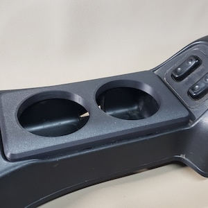 May include: Black plastic car center console with two cup holders and two black power window switches.