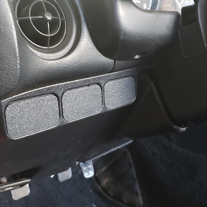 May include: Close-up of a car's interior with four black rectangular buttons with a textured surface.