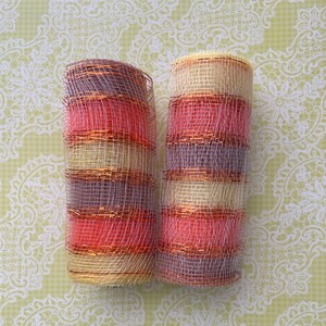 Pu&ograve; includere: Due rotoli di nastro decorativo a rete con un motivo a strisce in tonalit&agrave; di rosa, beige e viola. Il nastro &egrave; realizzato in un materiale a rete fine con un effetto metallizzato.