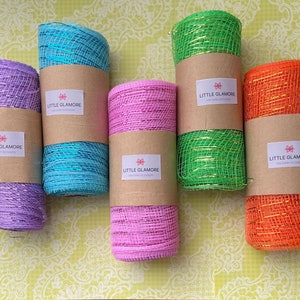 Pu&ograve; includere: Sei rotoli di nastro a rete metallica in vari colori, tra cui viola, verde acqua, rosa, verde e arancione. Ogni rotolo ha un'etichetta marrone con il testo "Little Glamore" e un piccolo disegno a stella.