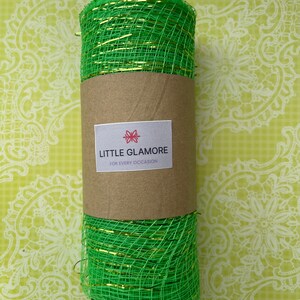 Pu&ograve; includere: Un rotolo di nastro in rete metallica verde e oro. Il nastro &egrave; avvolto attorno a un tubo di cartone marrone con un'etichetta che recita "Little Glamore for Every Occasion".