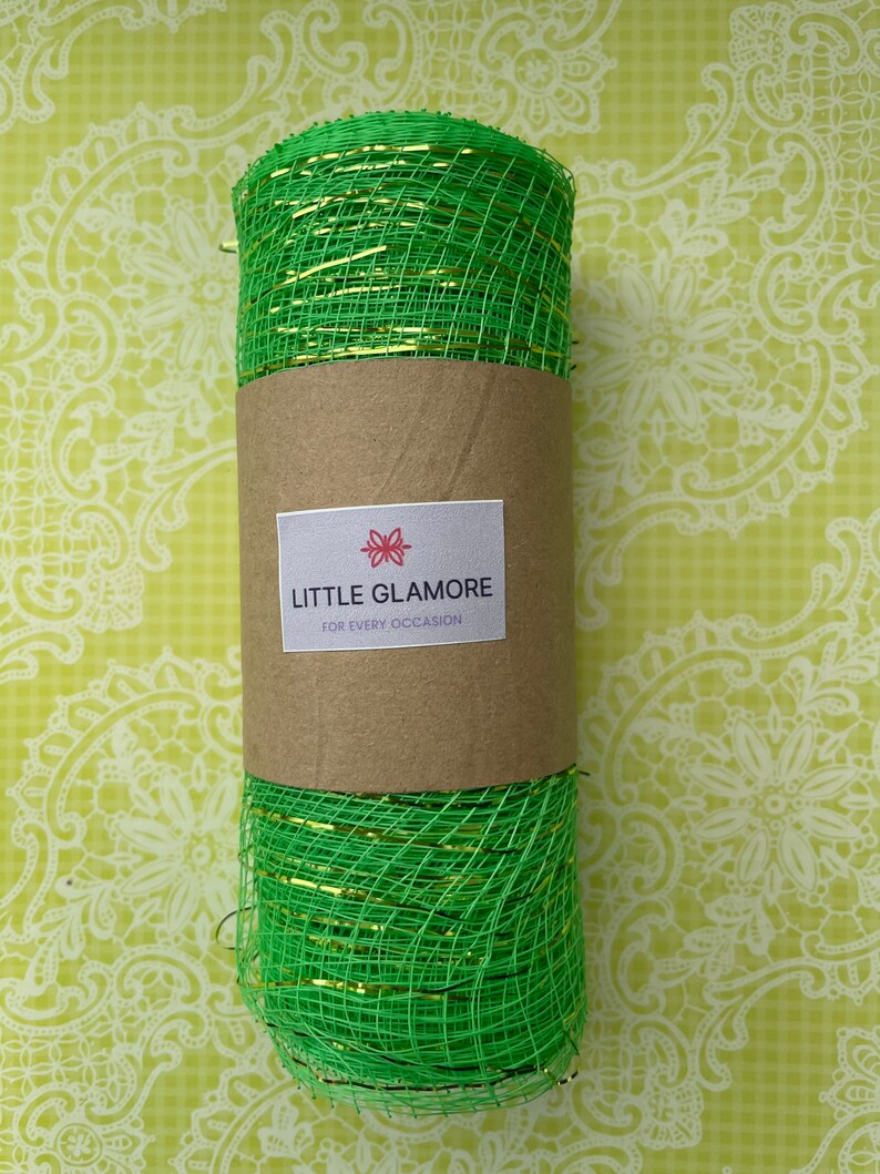 Pu&ograve; includere: Un rotolo di nastro in rete metallica verde e oro. Il nastro &egrave; avvolto attorno a un tubo di cartone marrone con un'etichetta che recita "Little Glamore for Every Occasion".