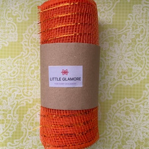 Pu&ograve; includere: Rotolo di nastro in rete arancione e oro con un'etichetta marrone che dice "Little Glamore for Every Occasion".