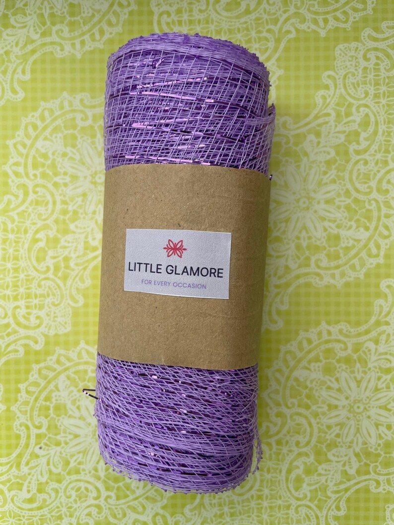 Pu&ograve; includere: Un rotolo di nastro di rete viola con un luccichio argentato. Il nastro &egrave; avvolto attorno a un tubo di carta marrone con un'etichetta che recita "LITTLE GLAMORE FOR EVERY OCCASION".