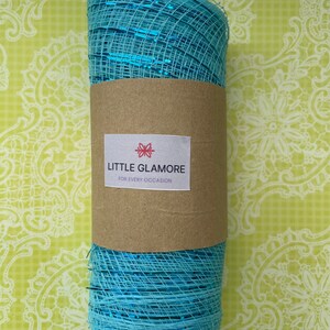 Pu&ograve; includere: Un rotolo di nastro in rete metallica blu con un'etichetta marrone su cui &egrave; scritto "LITTLE GLAMORE FOR EVERY OCCASION".