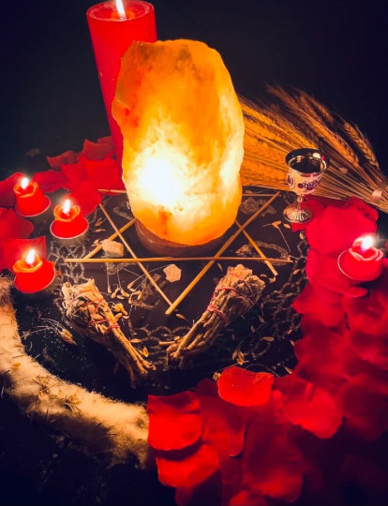 Pu&ograve; includere: Una scena mistica con una lampada di sale luminosa, candele rosse e petali di rosa sparsi. Due mazzi di salvia sono posti su una superficie scura, insieme a un calice d'argento e un disegno a forma di stella. L'atmosfera &egrave; arricchita da una luce soffusa.