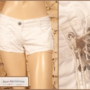 May include: White denim shorts with a lace-up detail on the sides. The shorts have a silver button and a label that reads "Jean's Paul Gaultier".