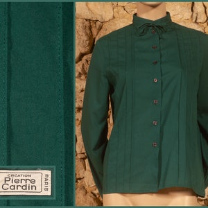 May include: A dark green long-sleeved shirt with a high collar and a button-up front. The shirt has a label that reads "Creation Pierre Cardin Paris" and "Made in France".