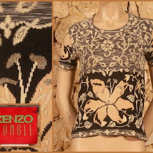 Peut inclure: Un t-shirt à manches courtes en tricot noir et beige avec un motif floral. Le t-shirt a un col rond et le texte "KENZO JUNGLE" est brodé sur une étiquette rouge.