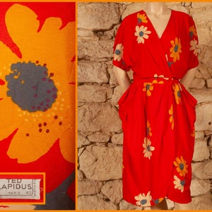 Könnte beinhalten: Ein rotes Wickelkleid mit weißen und gelben Blumenmustern. Das Kleid hat einen V-Ausschnitt, kurze Ärmel und einen passenden Gürtel. Das Bild zeigt auch eine Nahaufnahme des Stoffes mit einem großen Blumendesign. Das Kleid ist auf einer Schaufensterpuppe.