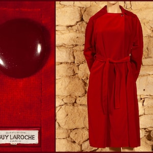 Könnte beinhalten: Ein langer, roter Samtmantel mit einem Bindegürtel. Der Mantel hat ein schlichtes, elegantes Design und ist aus einem luxuriösen Stoff gefertigt. Das Etikett auf dem Mantel lautet "Diffusion Guy Laroche Paris".