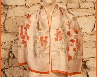 May include: A cream scarf featuring a floral design in orange, peach, and yellow hues. The scarf has an orange border and is draped over a mannequin. The scarf is made of a lightweight material, suitable for warmer weather.