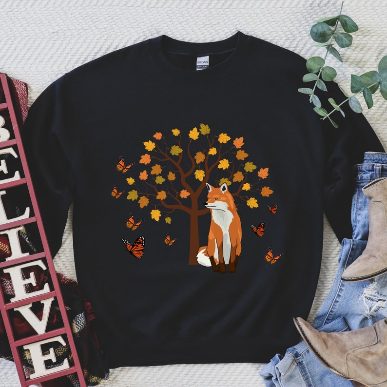 May include: Black sweatshirt with a graphic of a fox standing in front of a tree with orange and yellow leaves. Butterflies are flying around the tree.