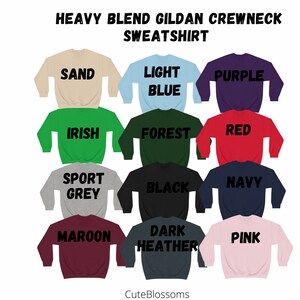 Puede incluir: Una selecci&oacute;n de sudaderas de cuello redondo en varios colores, incluyendo arena, azul claro, morado, verde irland&eacute;s, verde bosque, rojo, gris deportivo, negro, azul marino, granate, brezo oscuro y rosa. El texto "HEAVY BLEND GILDAN CREWNECK SWEATSHIRT" est&aacute; arriba.