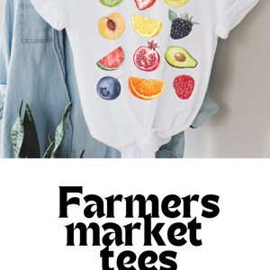 May include: White t-shirt with a colorful watercolor design of various fruits and berries. The text "Farmers market tees" and "Gifts for girls" is printed below the design. The text "CuteBlossoms/etsy" is printed below the text.