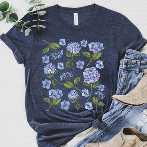 May include: A navy blue t-shirt featuring a watercolour print of blue hydrangeas and green leaves.