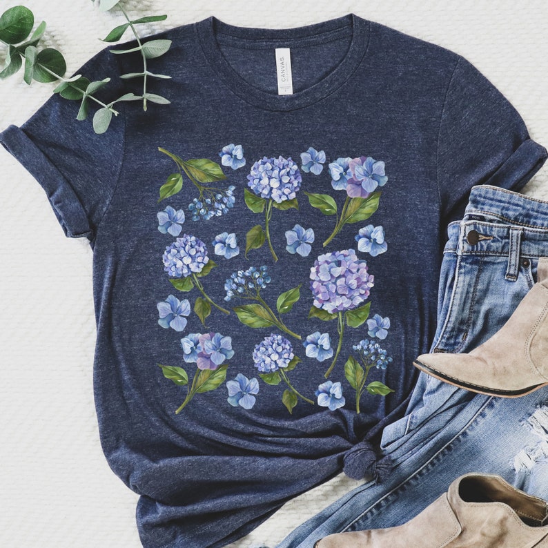 May include: A navy blue t-shirt featuring a watercolour print of blue hydrangeas and green leaves.