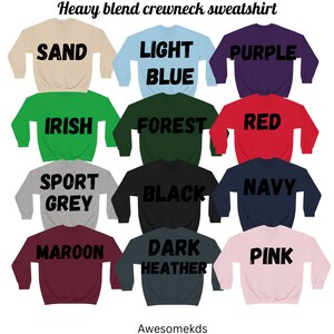May include: Twelve crewneck sweatshirts in various colors, including sand, light blue, purple, Irish green, forest green, red, sport grey, black, navy, maroon, dark heather, and pink. Each sweatshirt has a different color text on the back, including "SAND", "LIGHT BLUE", "PURPLE", "IRISH", "FOREST", "RED", "SPORT GREY", "BLACK", "NAVY", "MAROON", "DARK HEATHER", and "PINK".