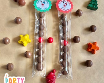 May include: Two clear plastic bags filled with chocolate candies, each with a green and red reindeer sticker that says "Reindeer Noises from Billy". The bags are surrounded by small chocolate candies, red and orange star-shaped crayons, and a green Christmas tree crayon.