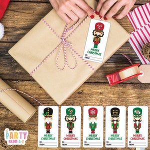 May include: A wrapped brown parcel tied with red and white twine, decorated with a Christmas gift tag featuring a cartoon nutcracker soldier. Additional nutcracker gift tags are displayed below. The tags read "Merry Christmas" and have space for "To:" and "From:" information.