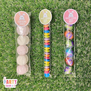 May include: Three clear cellophane bags filled with Easter treats. The bag on the left contains pink and white marshmallow eggs with a sticker that says "Cotton Tails". The middle bag contains a long string of colourful candy coated chocolate pieces with a sticker that says "Happy Easter from Billy". The bag on the right contains foil-wrapped chocolate eggs with a sticker that says "Happy Easter from Billy".