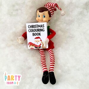 May include: A Christmas elf doll holding a small book that says "Christmas Colouring Book" with a picture of Santa Claus, a child, and a reindeer on the cover.