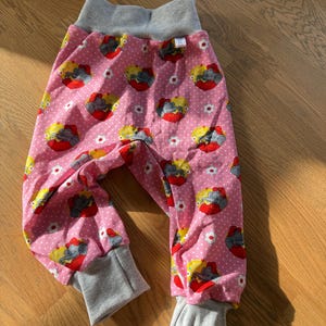 Könnte beinhalten: Rosa Babyhose mit einem sich wiederholenden Muster aus roten und gelben Elefanten. Die Hose hat einen grauen Bund und Bündchen. Weiße Punkte und kleine weiße Blumen sind auf dem Stoff verstreut.