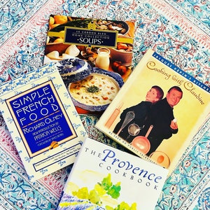 May include: A collection of four cookbooks with colorful covers. The books are titled "Simple French Food", "Le Cordon Bleu Home Collection Soups", "The Provence Cookbook", and "Cooking with Claudine".