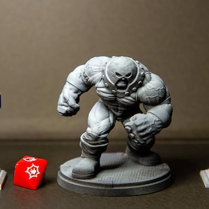 Può includere: Una statuetta in miniatura dipinta di grigio del personaggio dei fumetti Marvel, The Juggernaut, in piedi su una base grigia. La statuetta è in posa in una posizione di camminata con un braccio alzato e l'altro piegato al gomito. Un dado rosso con segni bianchi è in primo piano.