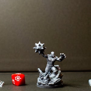 Peut inclure: Une figurine miniature grise d'un homme tenant une boule à pointes, debout sur une base grise. Il y a un lampadaire miniature gris et un feu de circulation miniature gris de chaque côté de la figurine. Un dé rouge se trouve devant la figurine.