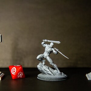Può includere: Una figura in miniatura grigia di un guerriero che tiene una spada, in piedi su una base di roccia grigia. La figura è circondata da un semaforo grigio, un dado rosso e un lampione grigio.
