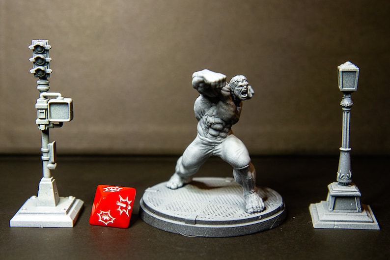 May include: A gray plastic miniature figure of the Hulk in a fighting pose, standing on a gray plastic base. The figure is surrounded by three gray plastic miniature street props: a traffic light, a street lamp, and a lamp post.