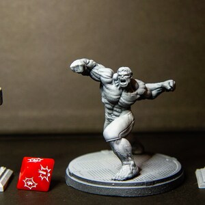May include: A gray plastic miniature figurine of the Hulk in a fighting pose. The Hulk is standing on a gray plastic base. There is a gray plastic streetlight and a gray plastic traffic light on either side of the Hulk. A red plastic dice with white spots is in front of the Hulk.