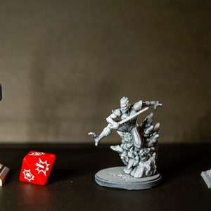 Peut inclure: Une miniature de lampadaire en plastique gris, un feu de circulation en plastique gris, un dé rouge avec des points blancs et une figurine miniature en plastique gris d'une personne tenant une épée.