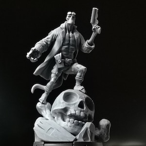 Può includere: Una statuetta dipinta di grigio di un personaggio di fumetti in piedi su un teschio. Il personaggio tiene una pistola in una mano e indossa un mantello e una cintura con una fibbia. Il teschio è dettagliato con denti e orbite.