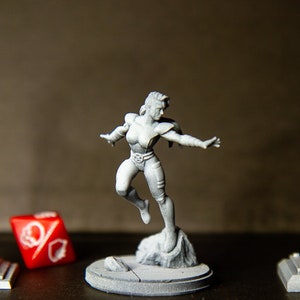 Peut inclure: Trois figurines miniatures : un lampadaire, une super-héroïne et un feu de circulation. Les figurines sont peintes en gris clair et sont posées sur une surface sombre.