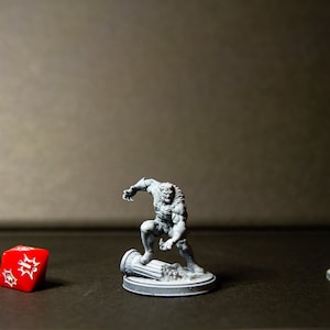 Peut inclure: Une figurine miniature grise de loup-garou debout sur une base grise. La figurine est posée en plein mouvement, les bras levés et les griffes tendues. La figurine est entourée d'une base grise avec un petit pilier gris. Un dé rouge avec des points blancs est au premier plan. Un lampadaire miniature gris et un feu de circulation miniature gris sont à l'arrière-plan.