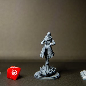 Peut inclure: Une figurine miniature grise d'une personne portant un manteau et une écharpe, debout sur une base avec un effet tourbillonnant. La figurine est devant un dé rouge à 20 faces et deux lampadaires miniatures gris.