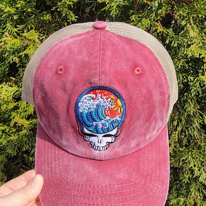 May include: A burgundy and beige trucker hat with a Grateful Dead Steal Your Face logo featuring a wave and sun design.