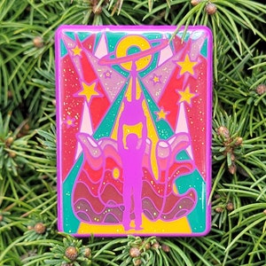 May include: A colorful enamel pin with a retro design featuring a person with raised arms standing in front of a wavy, multi-colored background with stars and a circle.