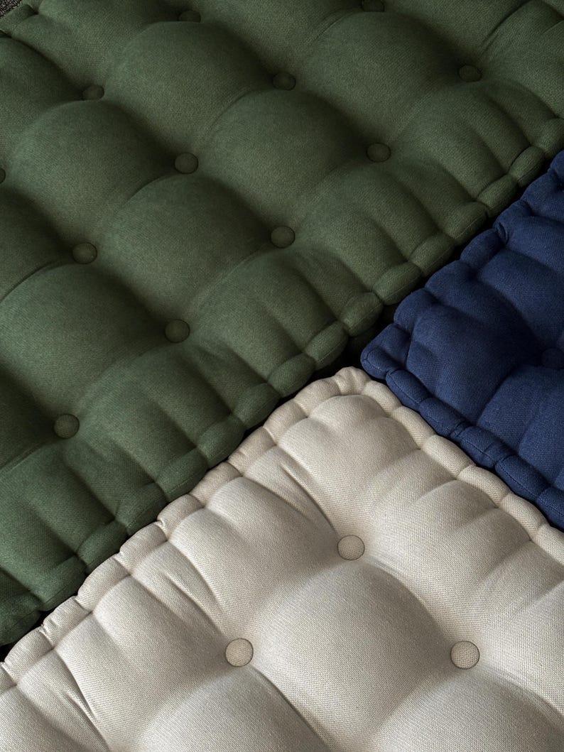 Close-up of tufted fabric cushions arranged diagonally, showing textured surfaces in olive green, off-white, and navy blue, with evenly spaced button details.
