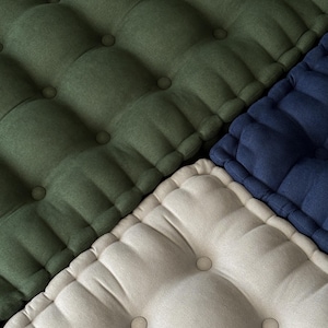 Close-up of tufted fabric cushions arranged diagonally, showing textured surfaces in olive green, off-white, and navy blue, with evenly spaced button details.