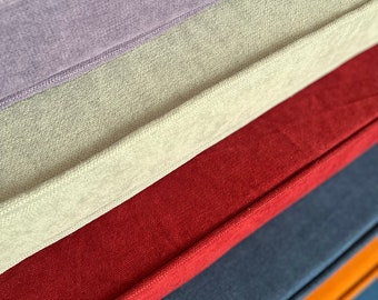 Peut inclure: Une pile de coussins rectangulaires dotés d'une finition en tissu doux et texturé. Les coussins sont disposés en diagonale, présentant une variété de couleurs dont le violet clair, le vert pâle, le rouge profond, le bleu foncé et l'orange vif.