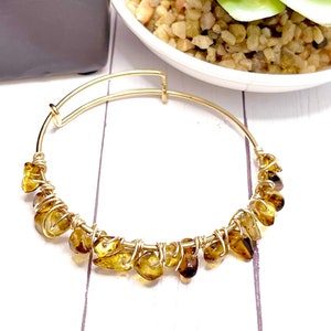 May include: A gold bangle bracelet with a cluster of small, irregular, brown and gold gemstones wrapped in gold wire.