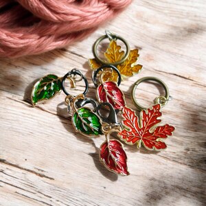 May include: Five colorful leaf-shaped stitch markers with gold metal rings. The markers are red, green, and yellow.