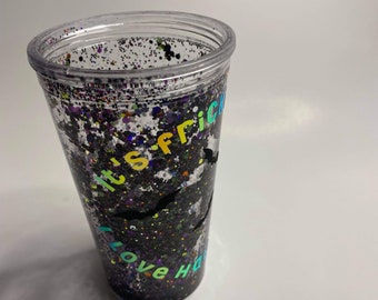 May include: Clear plastic tumbler filled with black glitter and colorful specks. The tumbler has the text "it's frickin' love Halloween" in rainbow colors. Two black bat silhouettes are also visible.