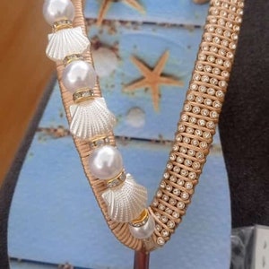 Op de afbeelding: Een paar blauwe slippers met een gouden band versierd met strass steentjes en witte schelpen met parel accenten.