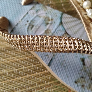 Op de afbeelding: Gouden flip-flop met een riem van strass en witte parelversieringen.