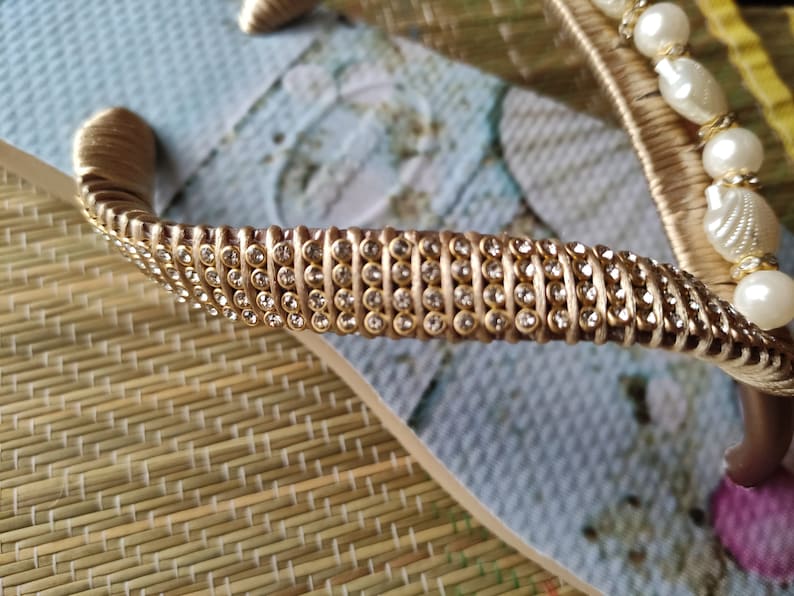 Op de afbeelding: Gouden flip-flop met een riem van strass en witte parelversieringen.