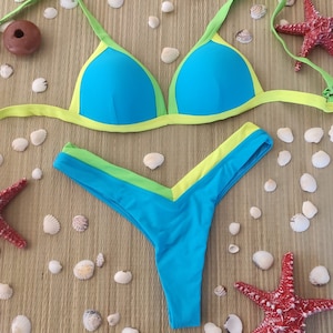 Könnte beinhalten: Ein türkisfarbener Bikini mit lindgrünem Besatz. Das Oberteil ist im Dreieckstil mit verstellbaren Trägern. Das Unterteil ist im frechen Stil mit hohem Beinausschnitt.